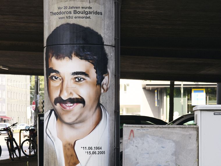 Foto eines Graffiti-Porträt eines bärtigen dunkelhaarigen Mannes mit weißem Hemd, das auf einen Brückenpfeiler gesprüht ist. Das Porträt ist überschrieben mit den Worten: "Vor 20 Jahren wurde Theodoros Boulgarides vom NSU ermordet." Zudem sind Geburtstag- und Sterbedatum zu lesen: "11.06.1954 – 16.06.2005".