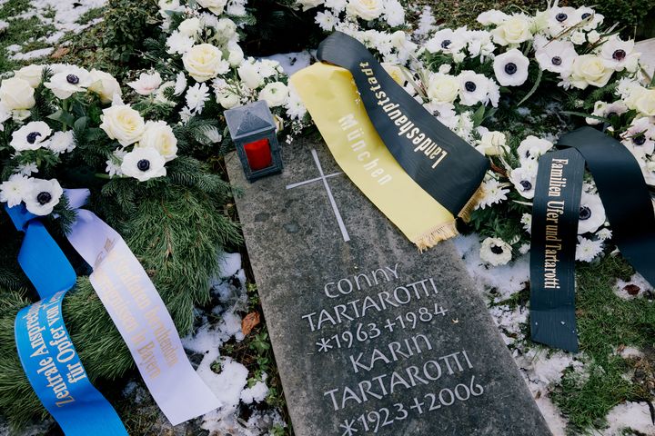 A horizontal gravestone with an inscription in metal letters. Several memorial wreaths have been laid around the grave.